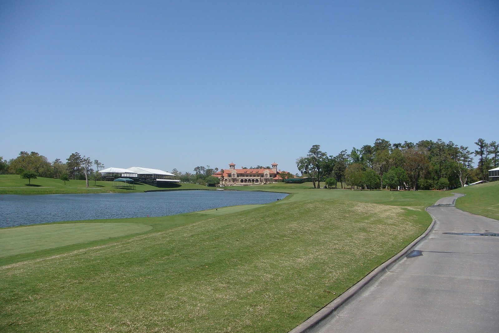 Golf course fairway and lake at TPC Sawgrass with a red tile roofed clubhouse and white hospitality tents in the distance